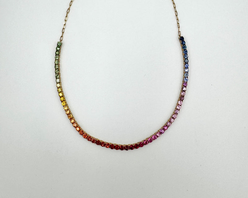 Necklace with multicolored sapphires on a gold chain on a light gray background